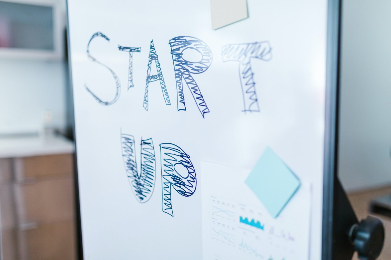 Ein Whiteboard, also eine Tafel zum Aufschreiben in Weiß, mit dem Schriftzug "Start up". Ein paar kleine Notizzettel und Postits sind auch noch mit dabei.