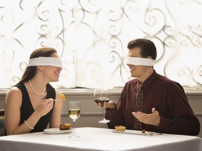 Mann und Frau sitzen am Tische haben Rot- und Weißwein und lernen sich mit verbundenen Augen kennen.