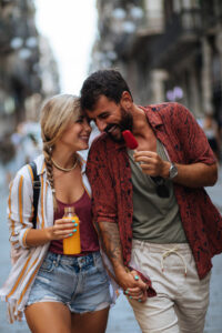 Ein glückliches Paar geht lachend auf einer Straße spazieren, während sie sich an den Händen halten. Sie genießen ein Eis und einen Saft.