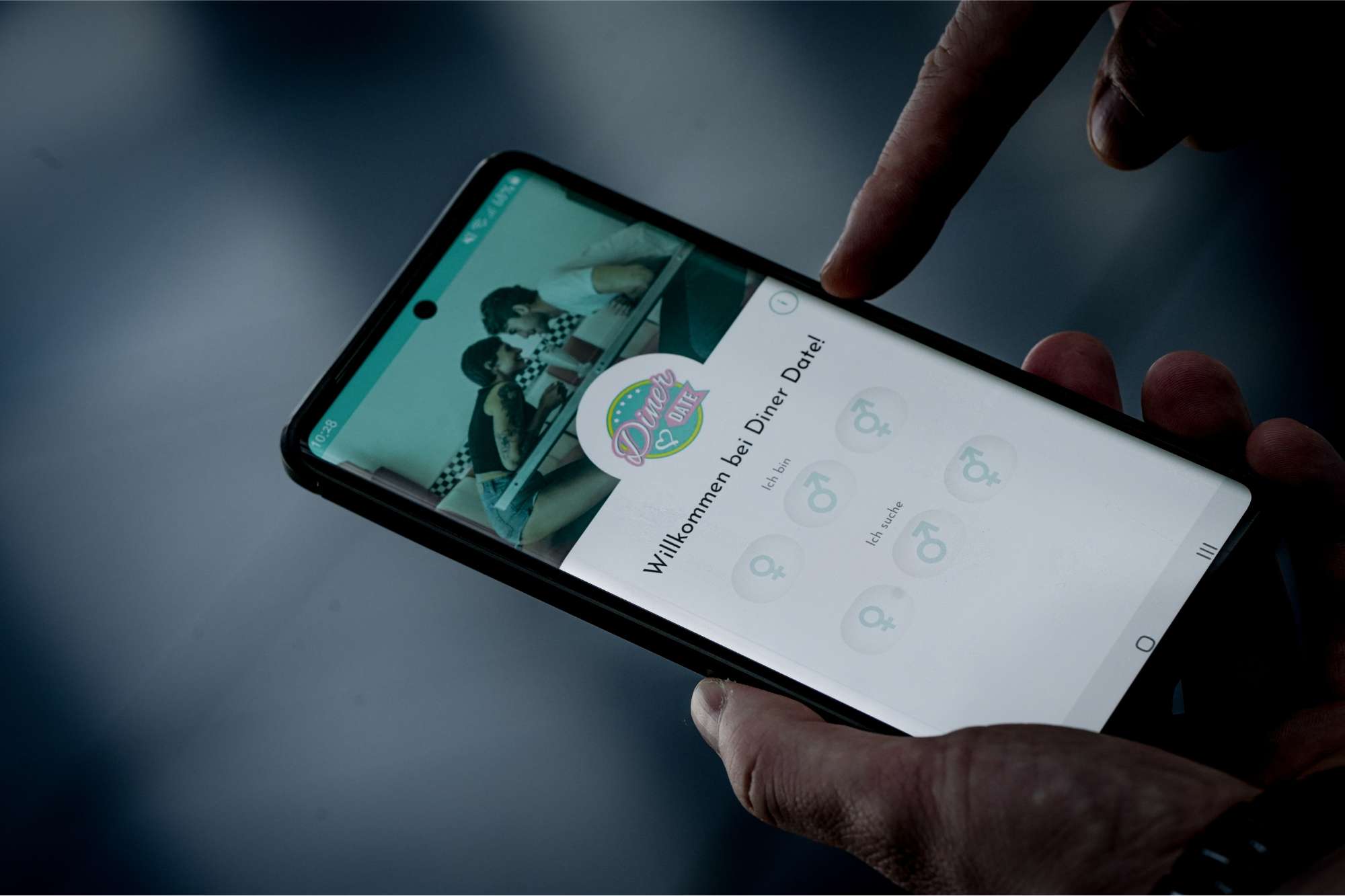 Hand zeigt auf ein Smartphone mit der neuen Dating-App „Diner Date“, die auf ehrliche und verifizierte Online-Dating-Erfahrungen setzt.