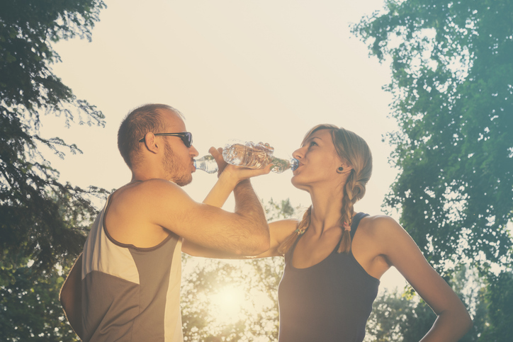 Junges Paar trinkt gemeinsam Wasser nach dem Training im Freien.