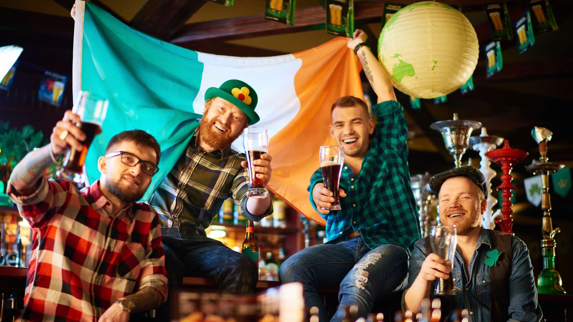 Vier Männer in einem irischen Pub, die mit Biergläsern anstoßen, während sie eine irische Flagge halten, eine gesellige Feier mit traditioneller Stimmung.