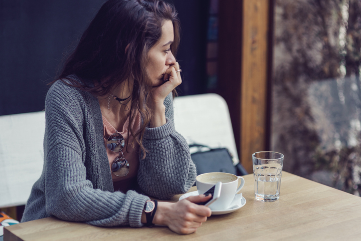 Nachdenkliche Frau sitzt allein im Café, symbolisiert Angst vor dem Alleinsein und Dating.