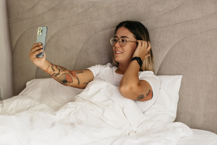 Frau macht ein Selfie im Bett, um neue Dating-Apps 2025 zu testen – Fokus auf kostenfreie Optionen.