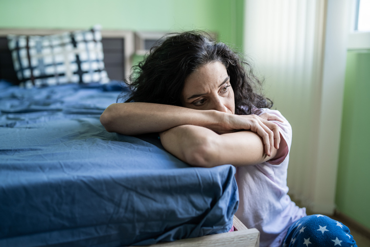 Nachdenkliche Frau sitzt an einem Bett, Symbol für Einsamkeit und Depression bei Singles.