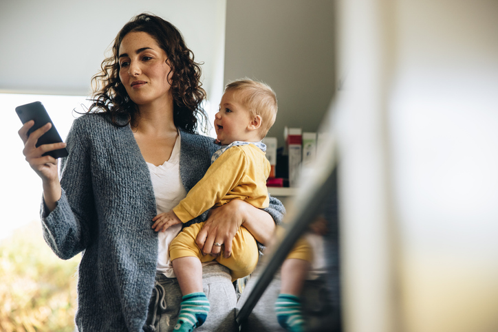 Alleinerziehende Mutter hält ihr Baby und schaut auf ihr Smartphone – ein Symbol für die Suche nach Balance zwischen Elternschaft und Dating-App-Nutzung.