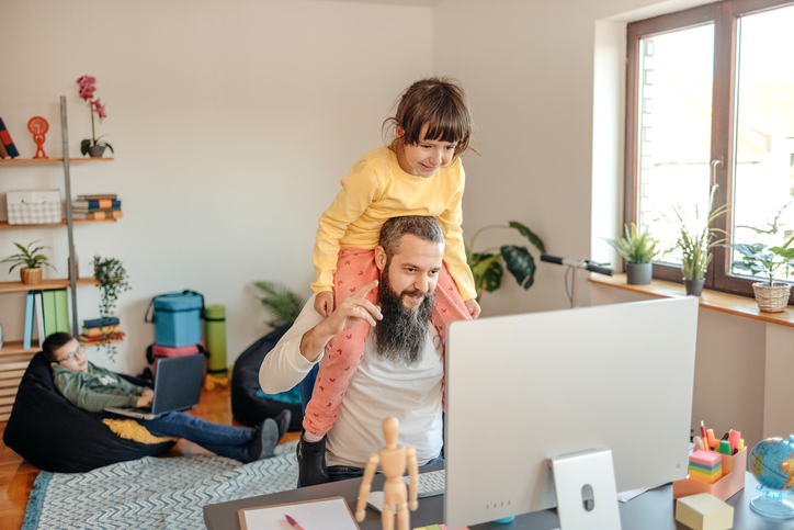 Alleinerziehender Vater arbeitet am Computer, während seine Tochter auf seinen Schultern sitzt – ein Einblick in den Balanceakt von Familie und Karriere.