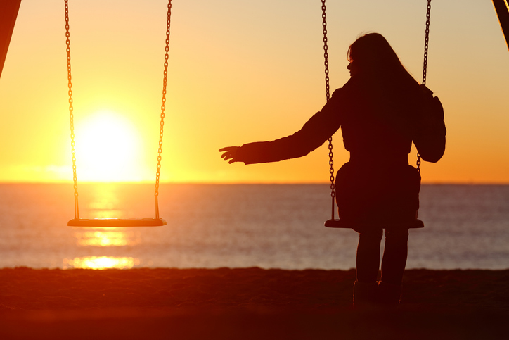 Single Frau sitzt alleine auf einer Schaukel am Meer und sehnt sich nach einem Partner, Symbolbild Einsamkeit.