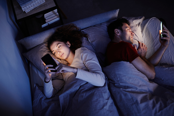 Frau und Mann im Bett, beide mit dem Handy in der Hand – Symbolbild für Cyber-Cheating und digitale Untreue in Beziehungen.