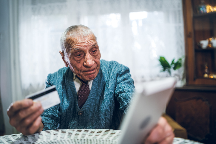 Älterer Mann hält eine Kreditkarte und schaut besorgt auf ein Tablet – Symbolbild für Abzocke bei unseriösen Partnervermittlungen