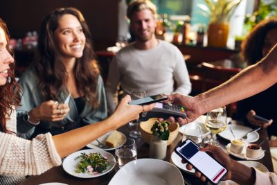 Freunde beim gemeinsamen Essen im Restaurant zahlen getrennt per Smartphone