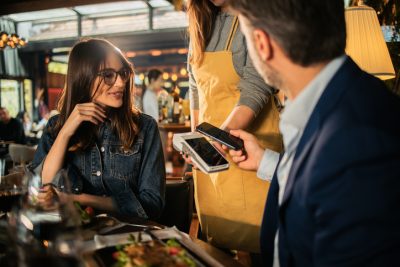 Mann zahlt beim Date kontaktlos, während Frau entspannt zusieht – Moderne Dating-Etikette