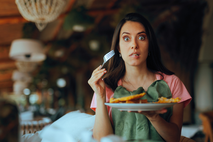 Überraschte junge Frau hält Teller mit Schnitzel und Gabel in der Hand, humorvoll geschockter Ausdruck zum Schniblo-Tag.