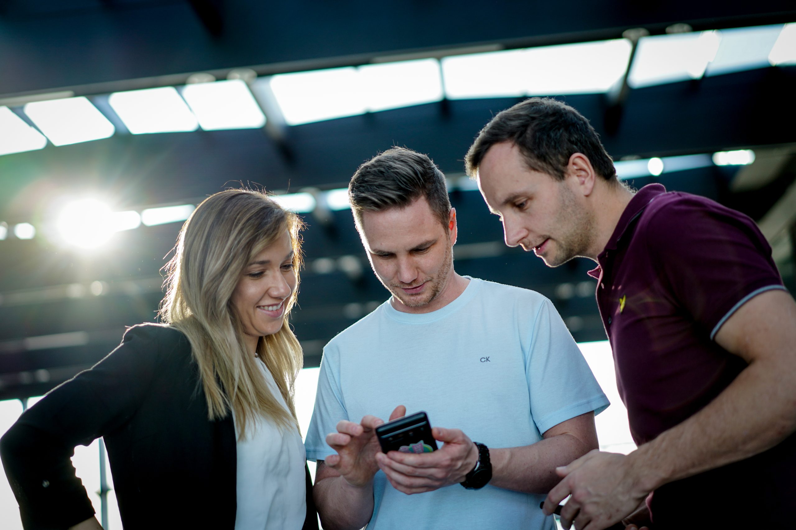Drei junge Menschen schauen gemeinsam auf ein Smartphone mit der Diner Date Dating App