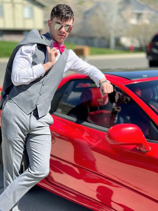 Junger Mann posiert mit Anzug vor rotem Sportwagen – Statussymbole im Dating