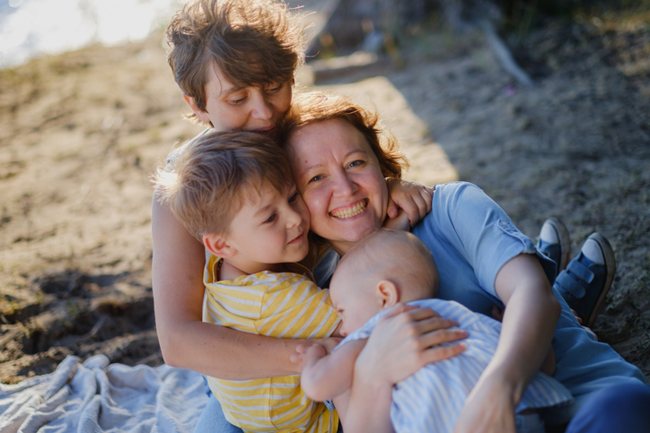 Zwei Frauen mit ihren Kindern beim Kuscheln am Strand – was Frauen am Muttertag wirklich brauchen: Nähe, Ruhe und echte Wertschätzung