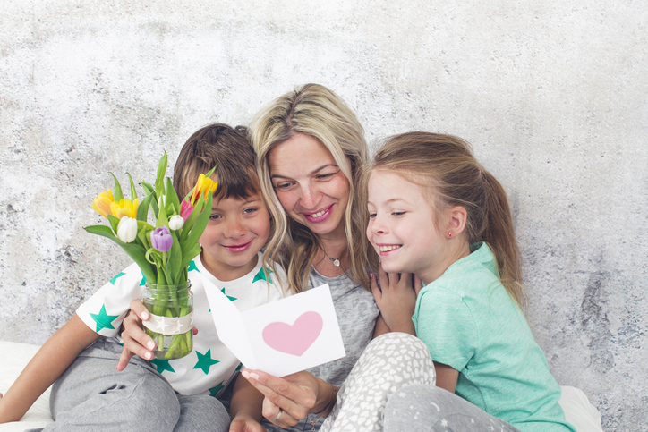 Mutter liest mit ihren zwei Kindern eine Karte zum Muttertag – Symbolbild für das, was Frauen am Muttertag wirklich brauchen: Wertschätzung, nicht nur Geschenke